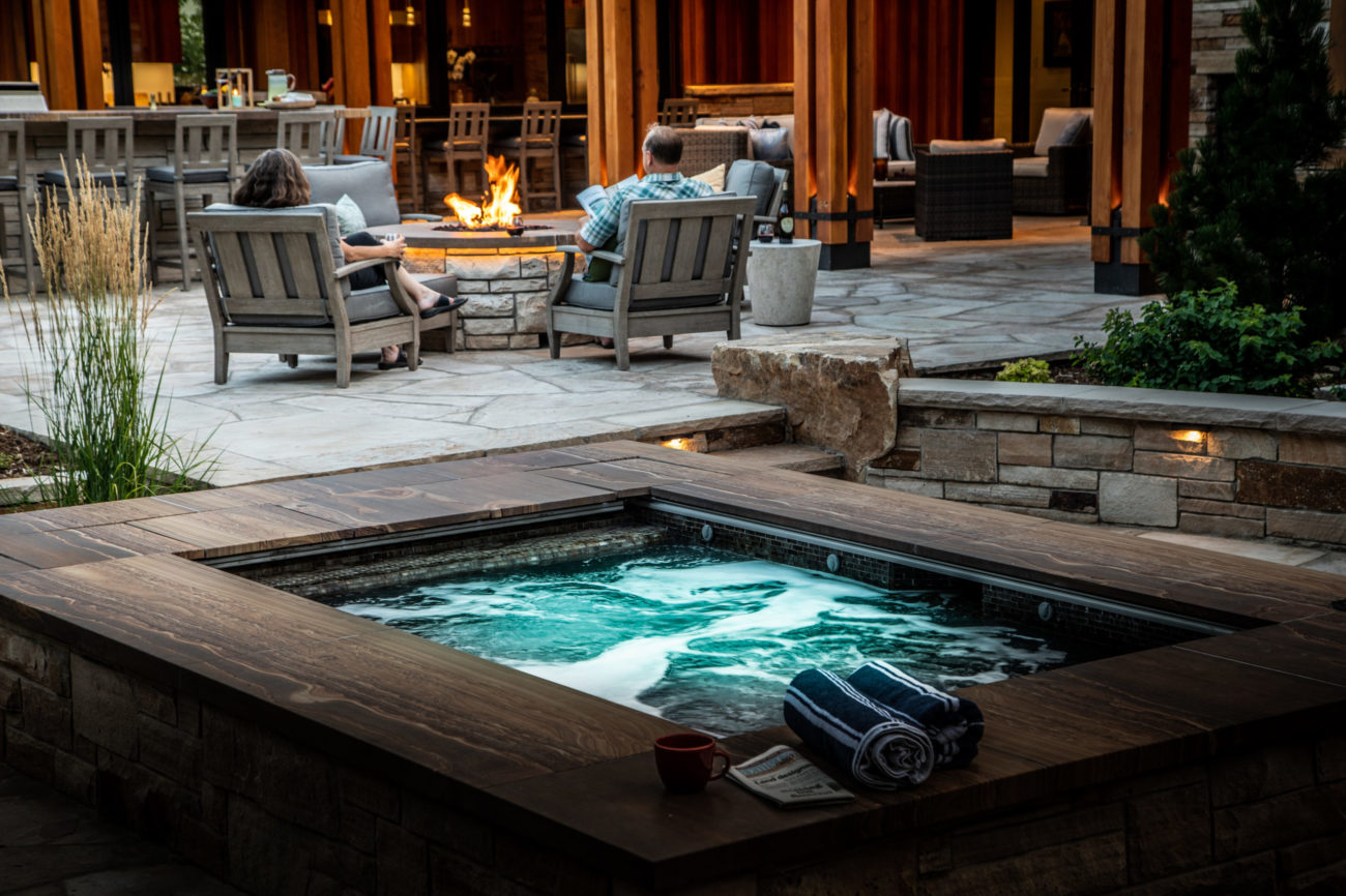 Outdoor living patio with hot tub and fire feature at sunset